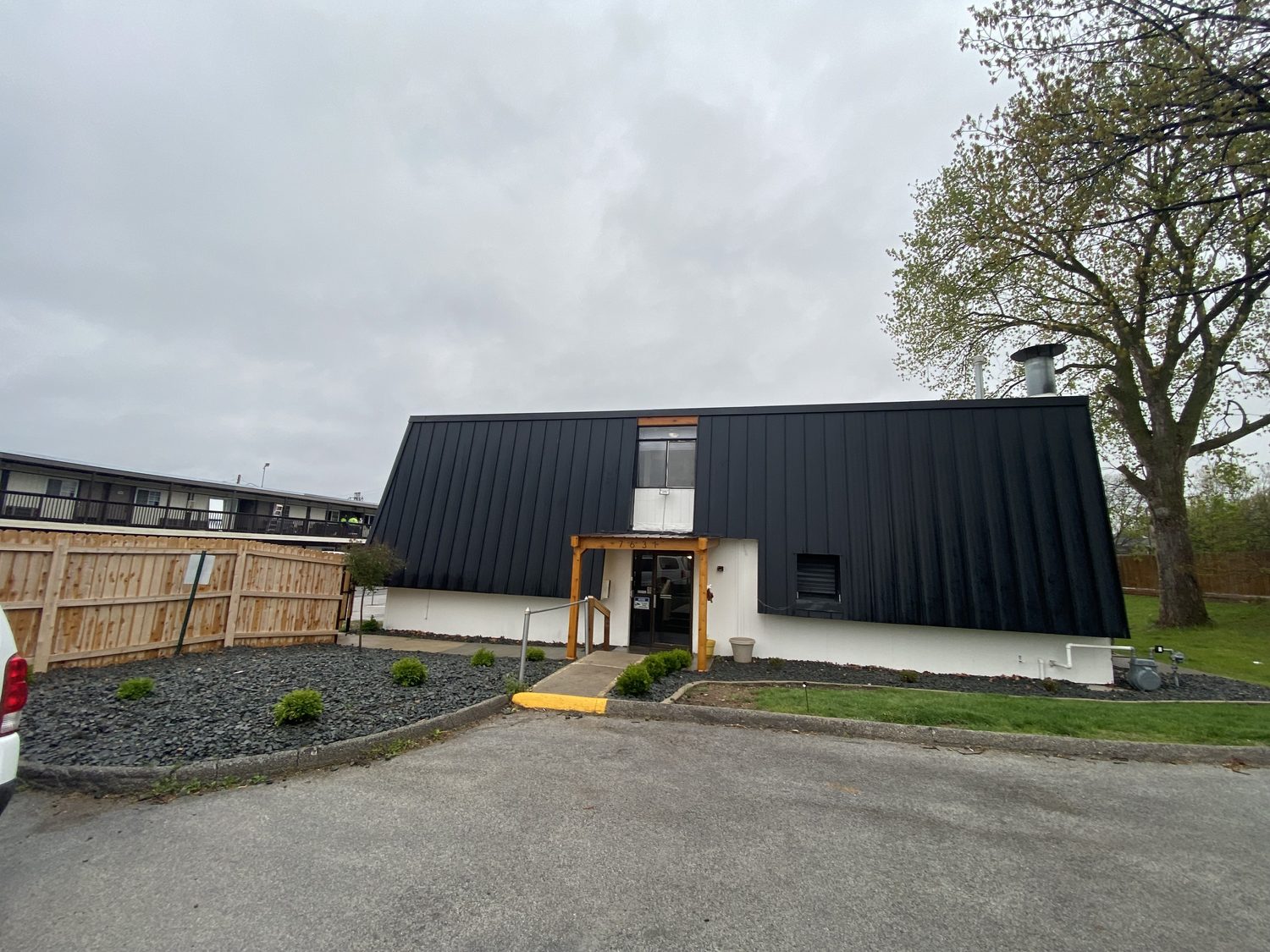 The front of Urban Heights from the parking lot, showing the black metal upper story, the cedar framed entry, the river rock beds and the cedar fence at the end of the building.