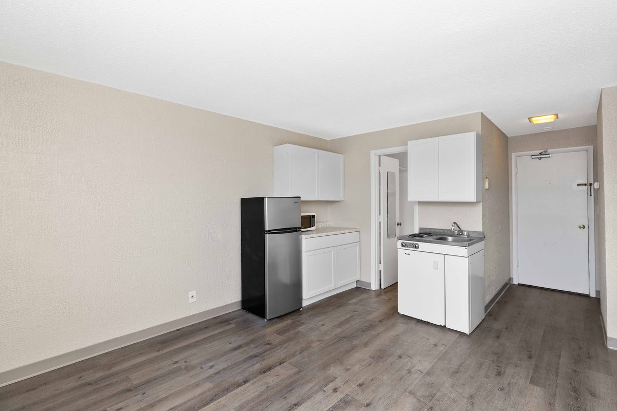 A renovated studio with the kitchen along one wall, white cabinets, a refrigerator and a range, and plank flooring running to the entry door.