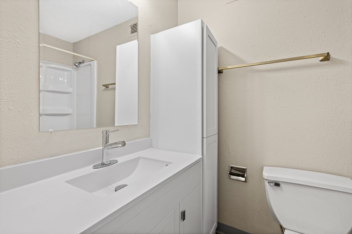 A renovated bathroom with a white vanity, a tub and shower, and a wall mirror above the sink.