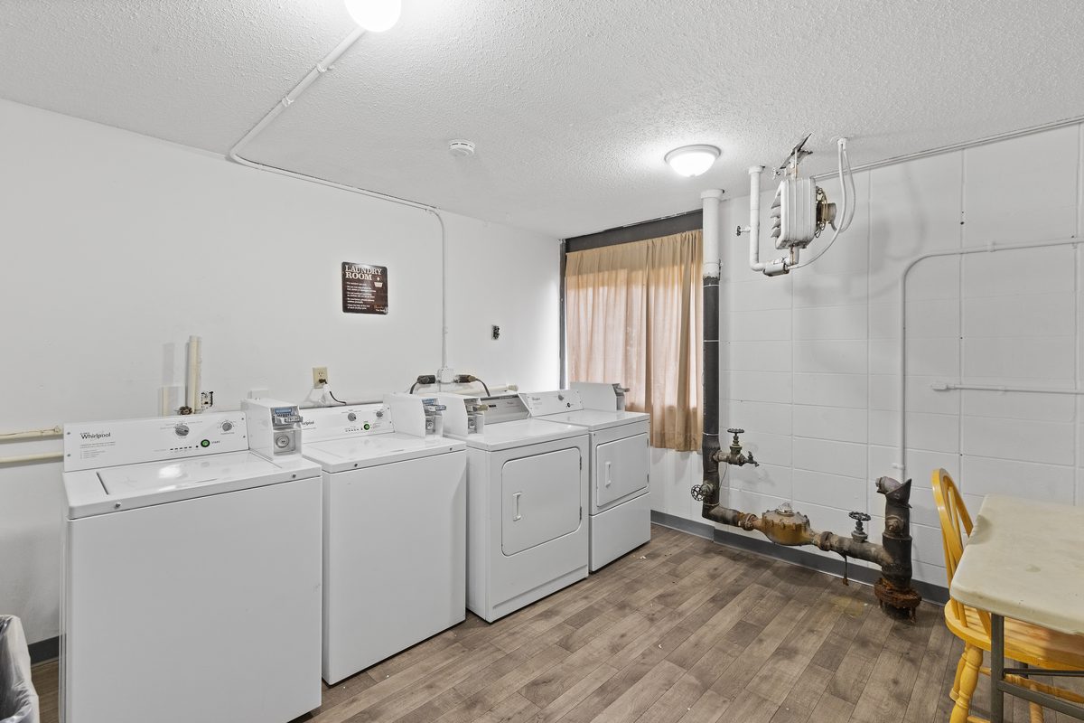 The laundry room with three washers and dryers along the wall, plank flooring and a table and chair.