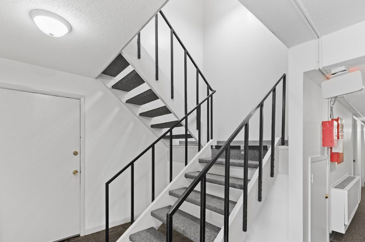 The main entry stairwell, painted white, with a black steel stair rail and new ceiling lighting.