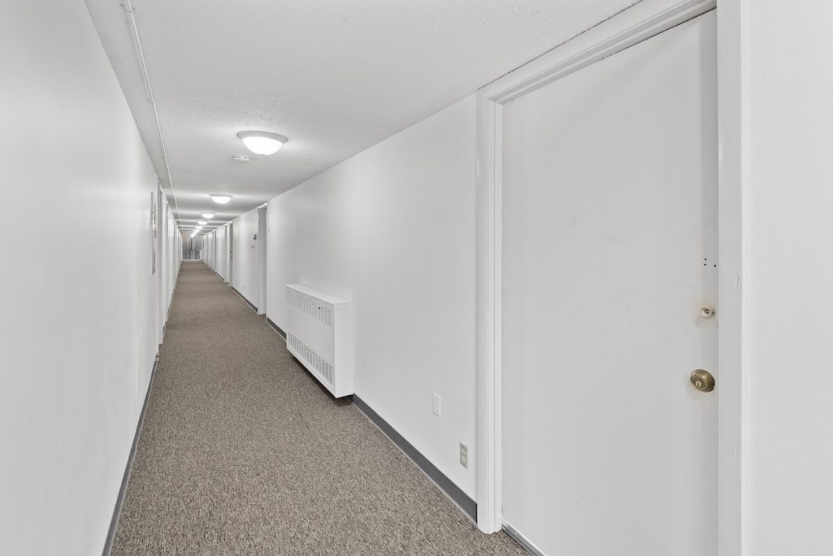 An interior hallway running the length of the building, with white walls and apartment doors on both sides.