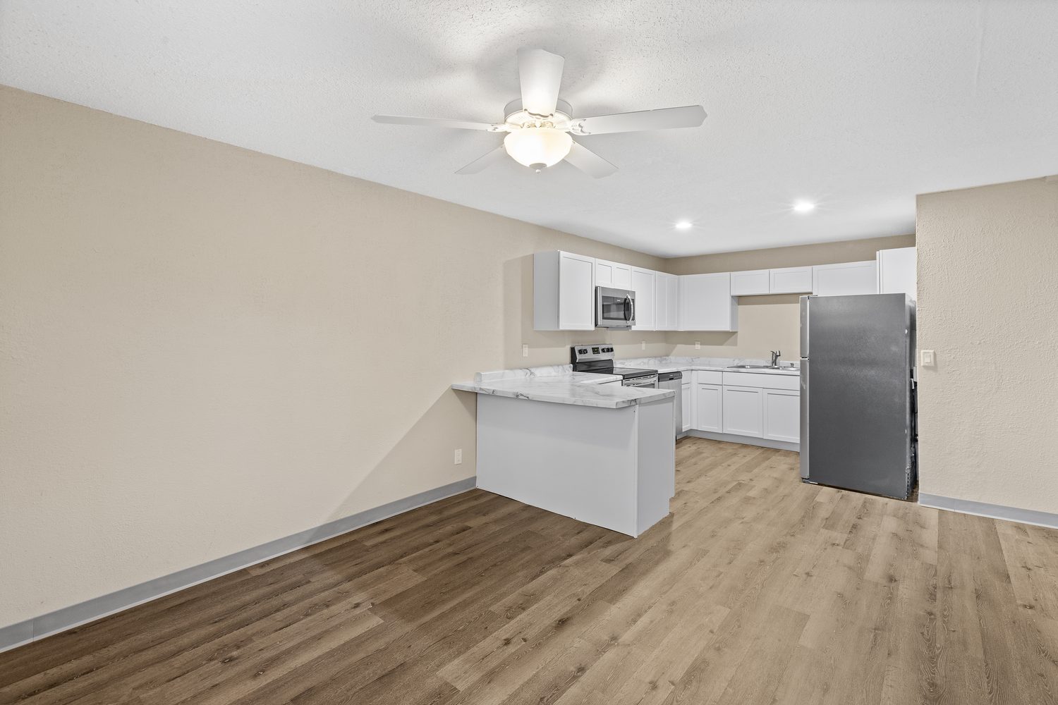 A renovated apartment at Urban Heights with wood-look plank flooring, a white kitchen with a stainless refrigerator and range at the back wall, and a ceiling fan overhead.